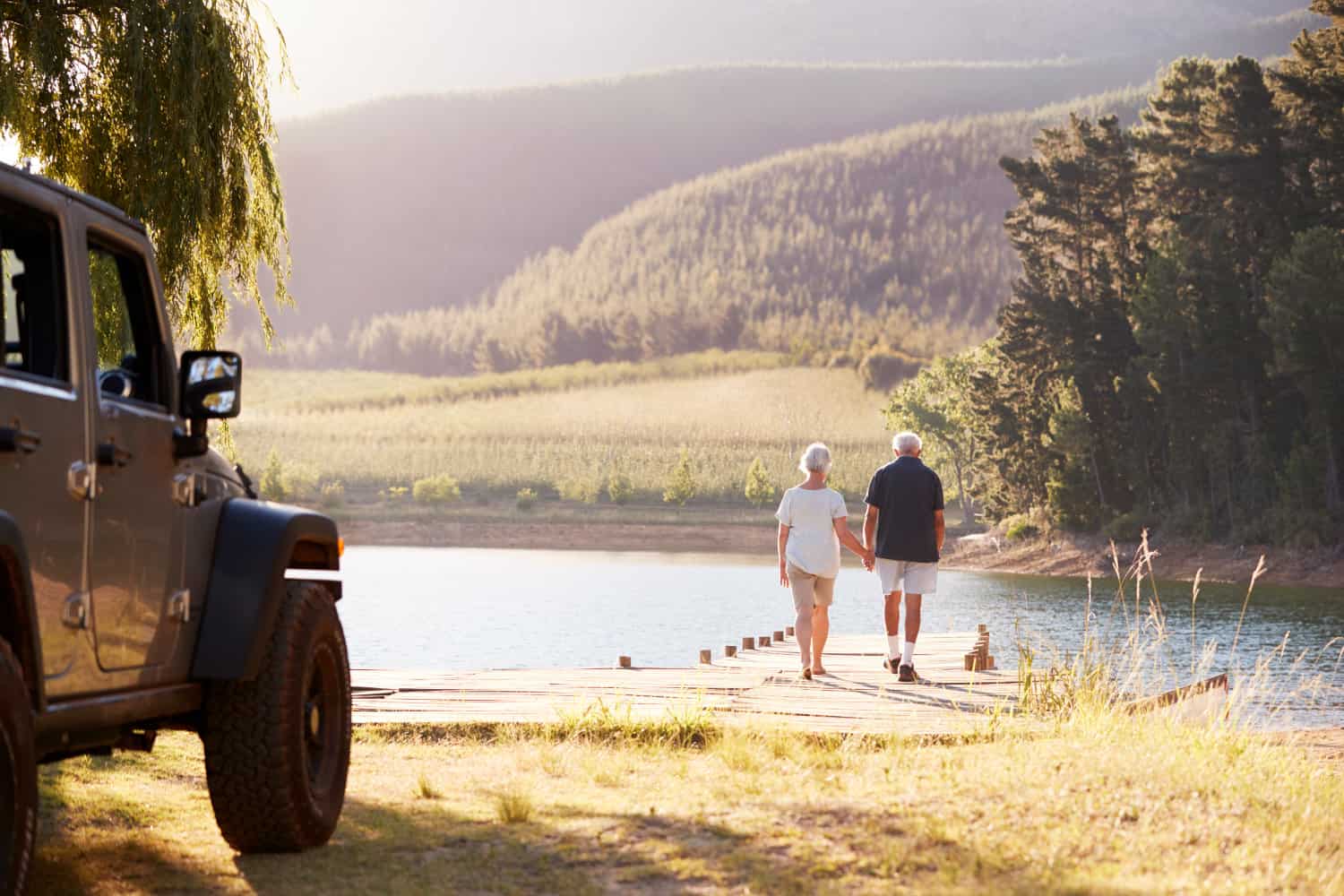 Retired couple walking from their Jeep to a pier on the water