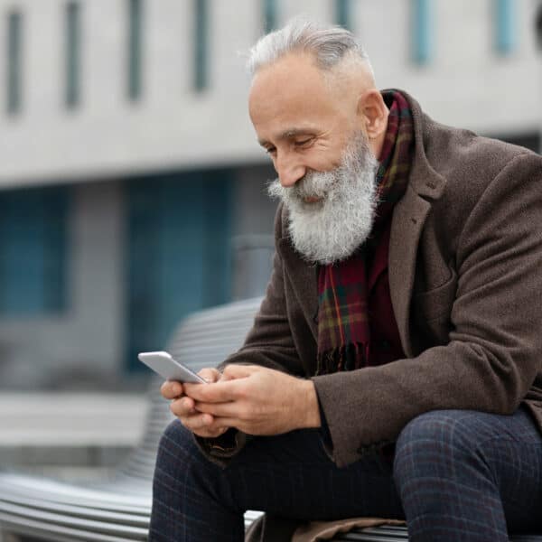Happy elderly man using smartphone while resting on street